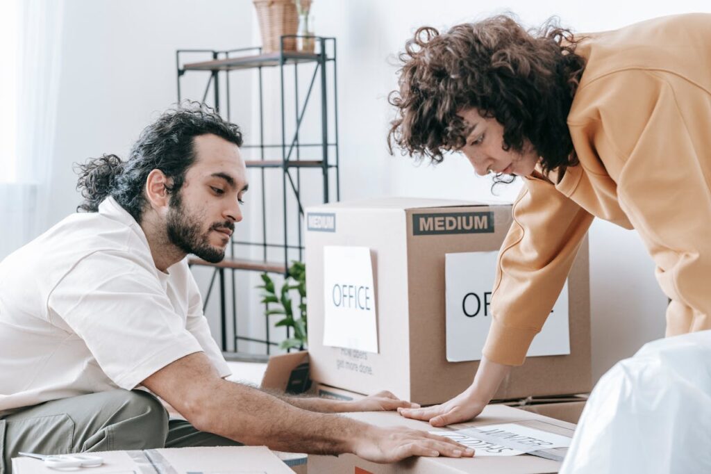 A couple packing and organizing office supplies into labeled boxes, preparing for relocation.