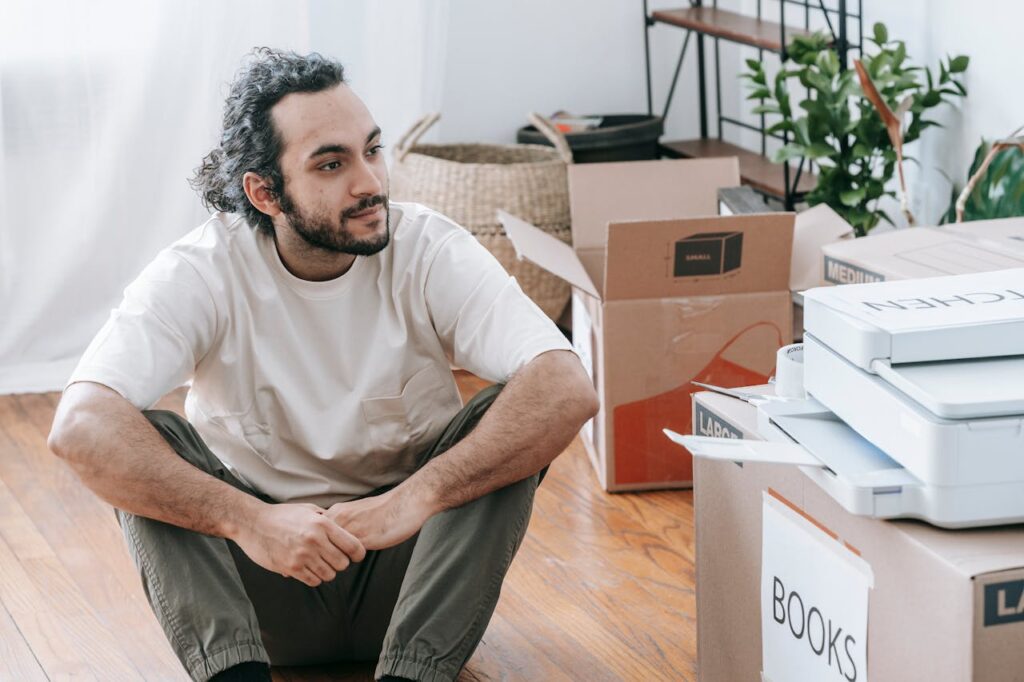 A man sitting on the floor surrounded by boxes, contemplating and organizing during a move.