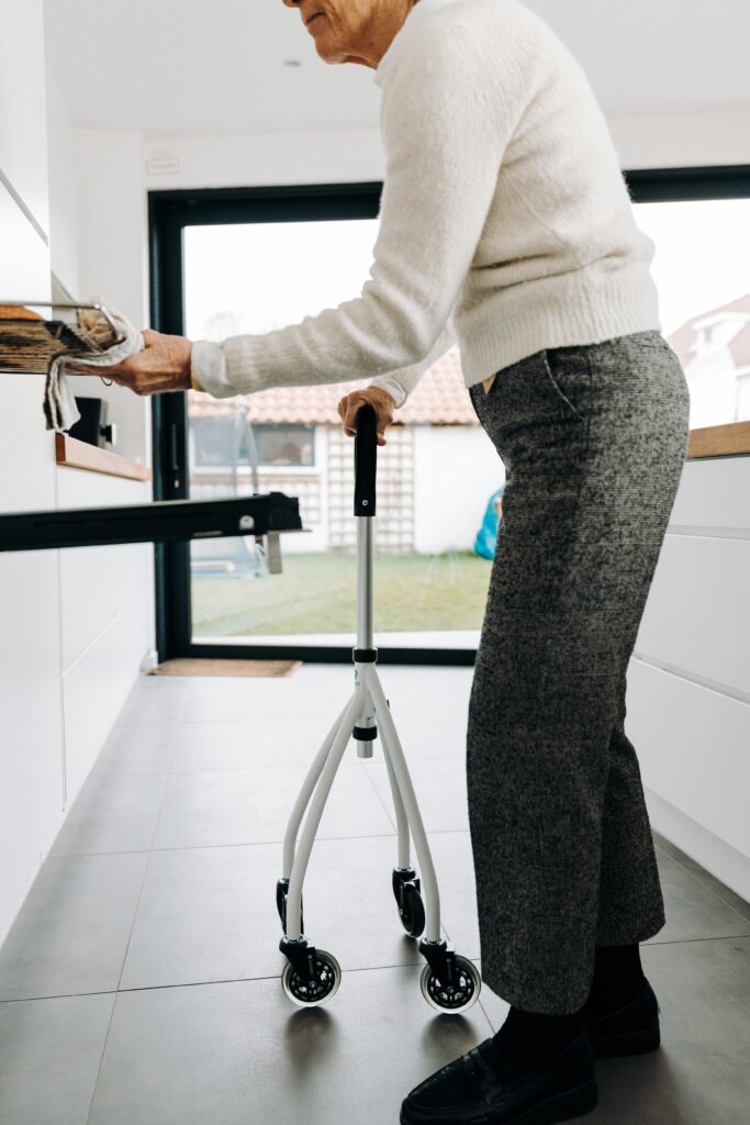 Elderly woman using a walker to assist with mobility in a bright, modern kitchen setting.