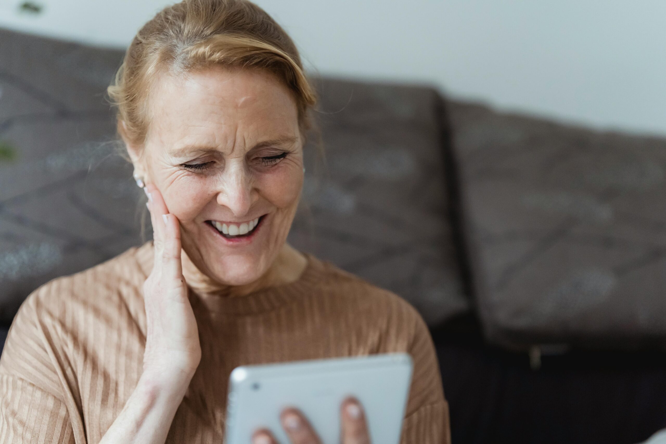 A senior woman with a warm smile using a tablet indoors, enjoying a moment.