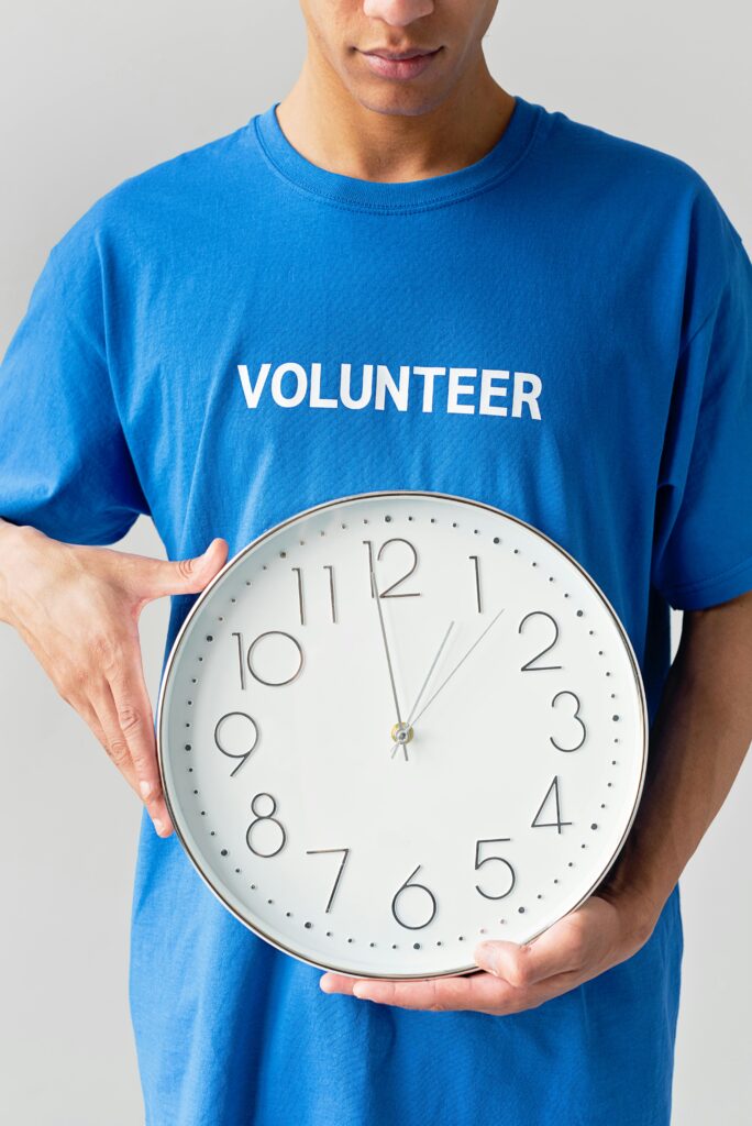 Person in blue shirt holding wall clock, emphasizing time and volunteerism.