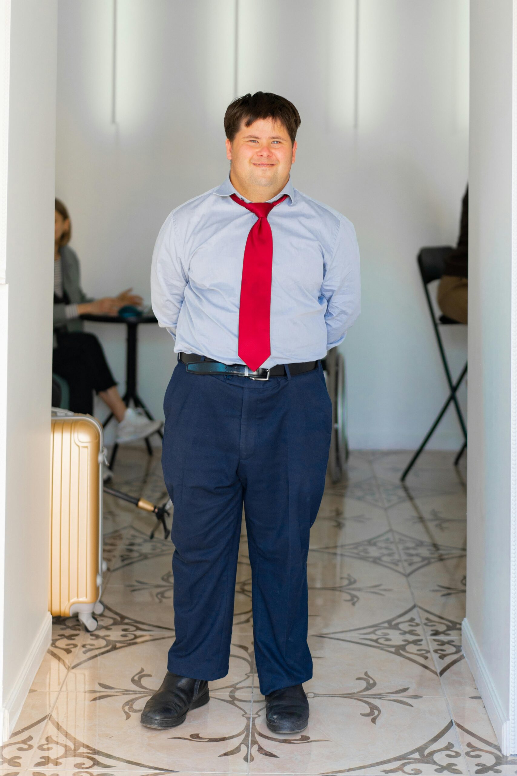 A man in formal attire with a red tie, smiling confidently indoors.